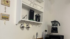 A compact kitchen with a built-in sink, a microwave, and a coffee maker. There are two shelves above the sink, one holding a box and the other holding a few items.
