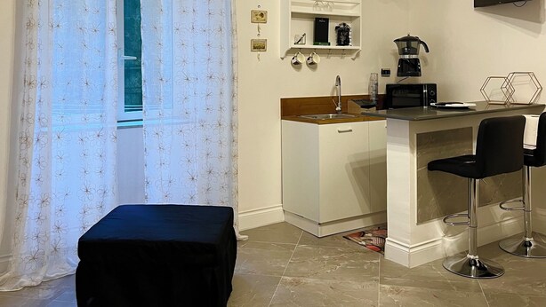 A modern kitchen with a bar area, a large window with floral curtains, and a flat-screen TV mounted on the wall.