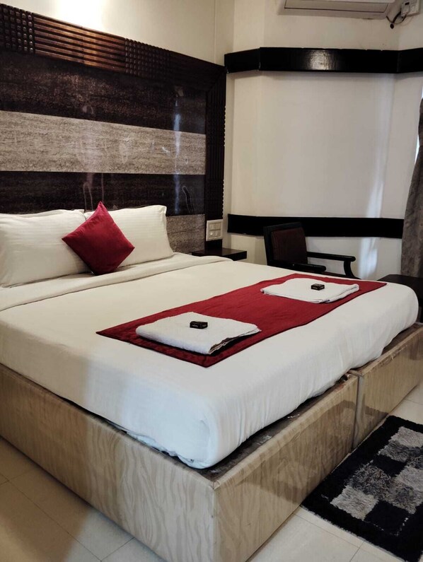 A hotel room with a large bed, a wooden headboard, a red pillow, a white blanket, and a black and white rug.