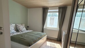 Et moderne soveværelse med trægulv, seng med blomsterpuder, loftslampe og et vindue med gardiner.