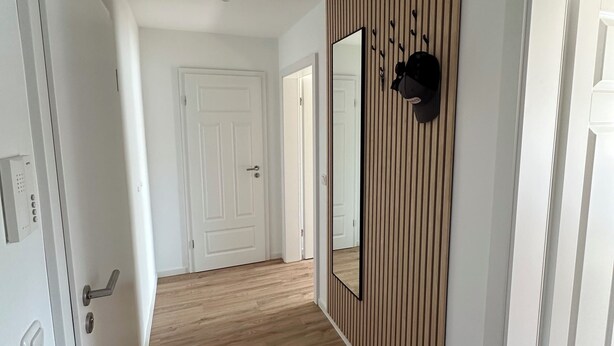 En gang med trægulv, hvide vægge og et stort spejl på den ene side.