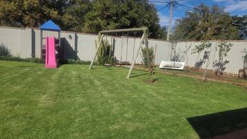 A backyard with a swing set, a small playhouse, and a cactus.