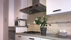 A modern kitchen with white cabinets, a microwave, a gas stove, and a potted plant. - Stella apartment 10 min. from Venice (Venezia)