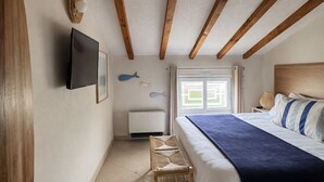 Um quarto com cama, televisão, janela e uma mesinha.