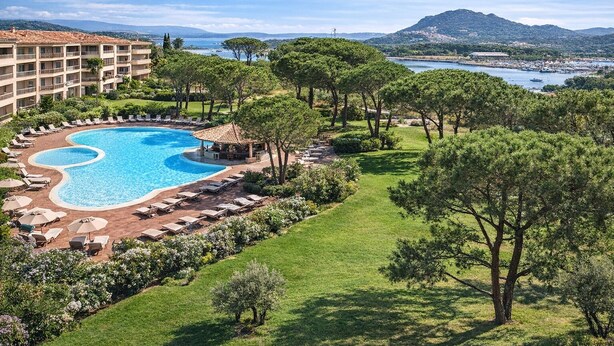 Um resort com uma grande piscina, espreguiçadeiras e vista para o mar e as montanhas.