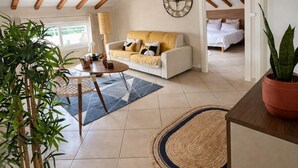 Uma ampla sala de estar com teto alto, vigas de madeira aparentes, um sofá, uma mesa de jantar e um vaso com planta.