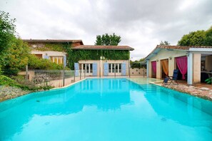Une piscine à l’eau d’un bleu cristallin, entourée d’un espace clos par une clôture, où se trouvent une maison et un coin salon abrité.