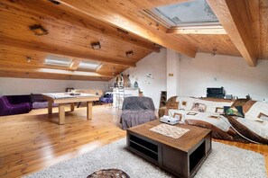 Een ruime loft met een hoge nok, houten balken, dakraam, een eethoek en een gezellige zithoek met een bank en salontafel.