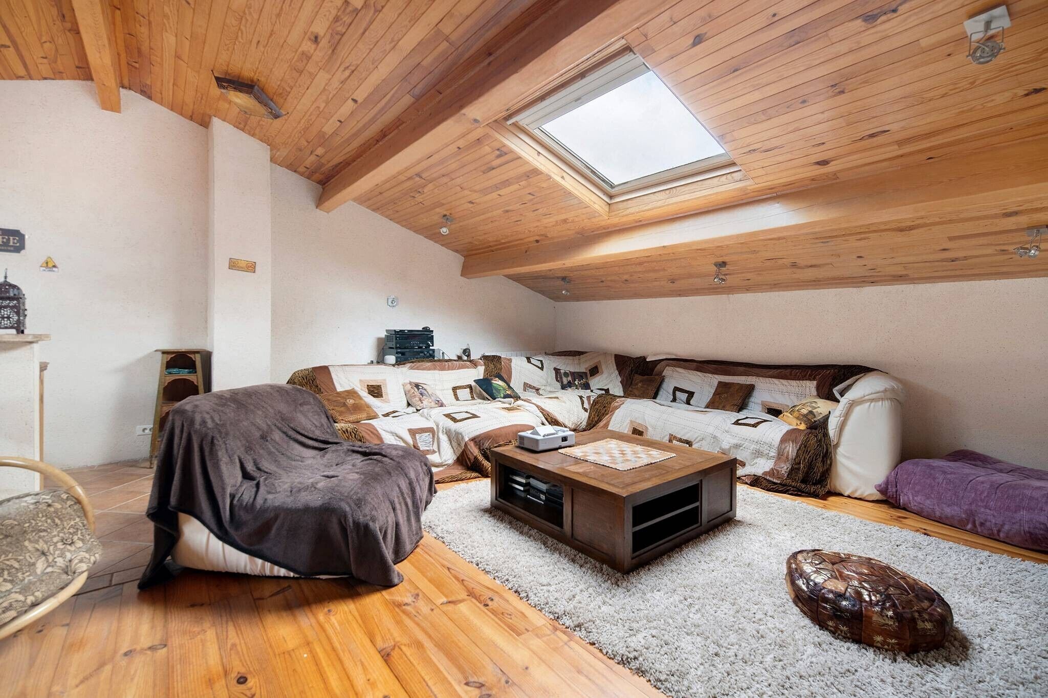 Un salon chaleureux de style loft, doté d’un plafond haut, de poutres en bois, d’une lucarne, d’un ensemble de canapés, d’une table basse et d’un petit tapis.
