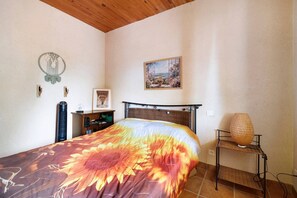 Een slaapkamer met een bed, een nachtkastje, een lamp, een foto aan de muur en een raam.