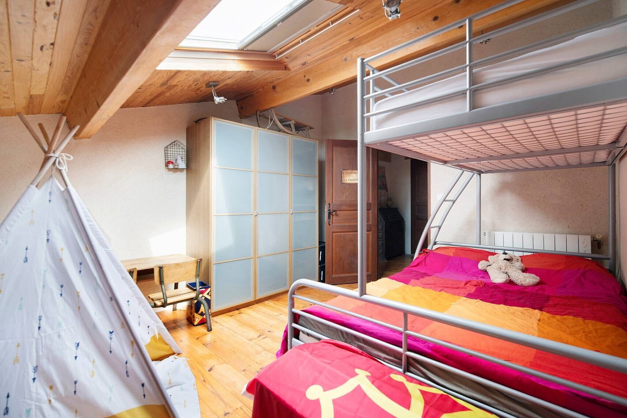 Ein Schlafsaalzimmer mit Etagenbetten, einer Holzbalkendecke, einem Fenster und einem kleinen Tisch mit Stuhl.