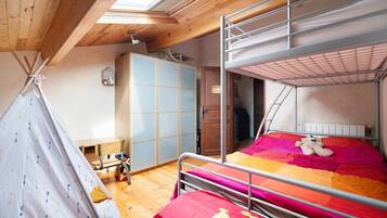 Ein Schlafsaalzimmer mit Etagenbetten, einer Holzbalkendecke, einem Fenster und einem kleinen Tisch mit Stuhl.