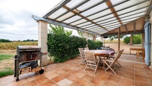Een terras buiten met een barbecue, houten stoelen en een tafel.