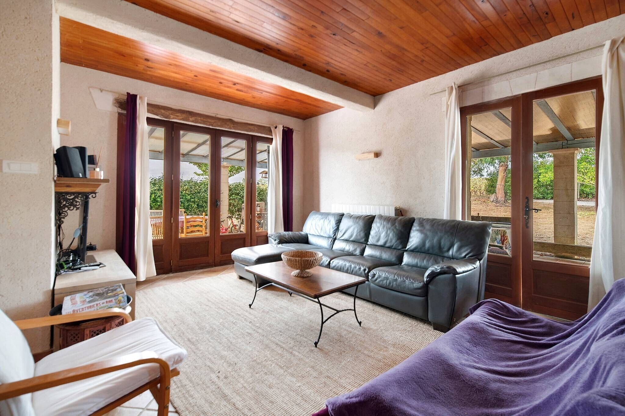 A living room with a leather sofa, a wooden coffee table, and a window with a view of greenery.