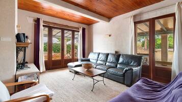 A living room with a leather sofa, a wooden coffee table, and a window with a view of greenery.