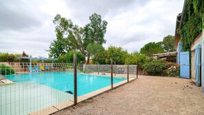 Une piscine entourée d’une clôture, de gravier, d’arbres et d’un bâtiment doté d’une porte bleue.