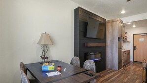 A dining area with a wooden table, chairs, a lamp, and a television mounted on a dark wall.