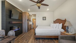 A hotel room with a bed, a desk, a chair, a TV mounted on the wall, and a ceiling fan.