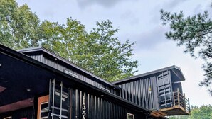 Un bâtiment en métal noir, doté d’un toit plat et d’une terrasse en bois.