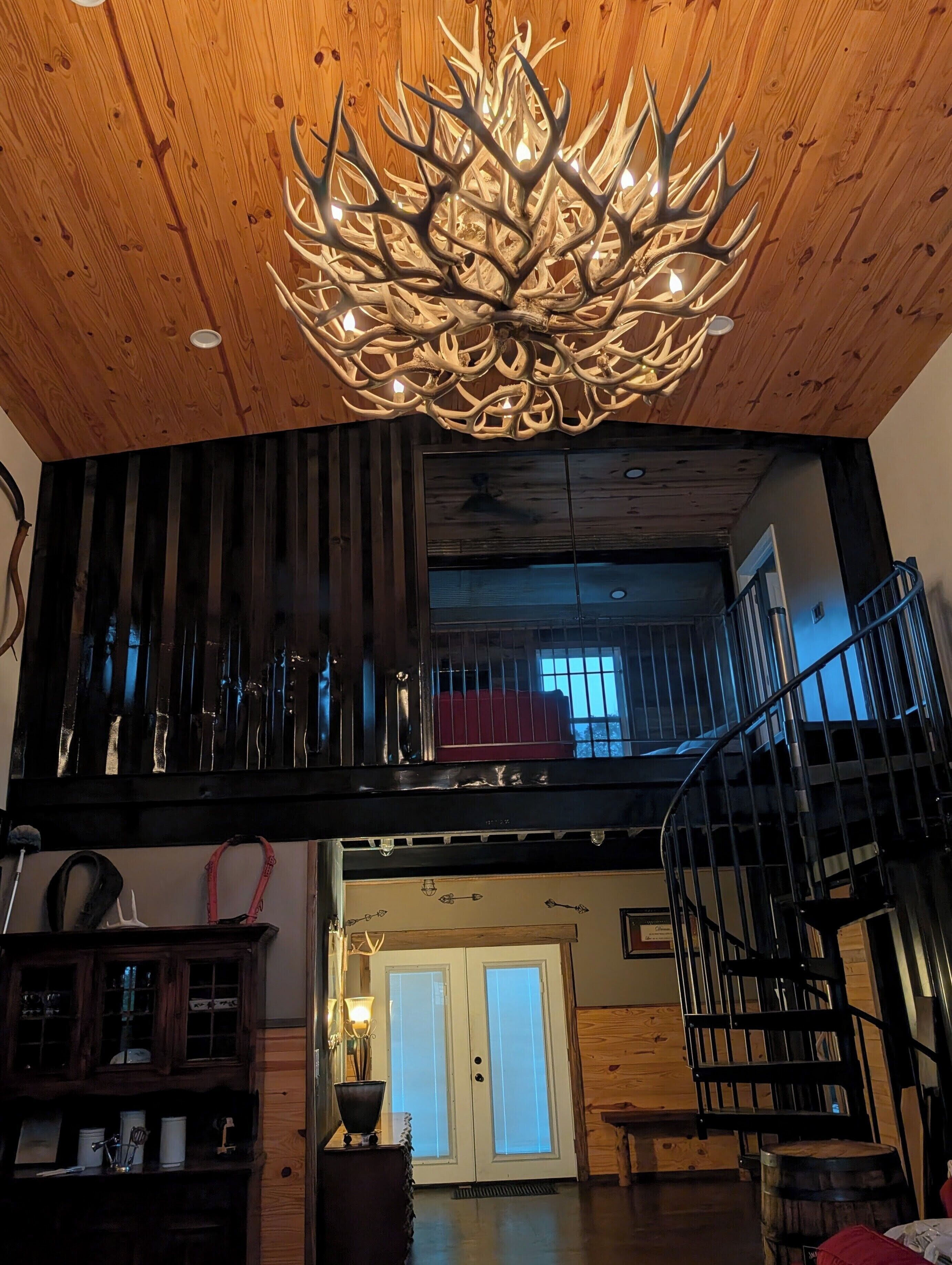 A chandelier with antler-like branches, a wooden ceiling, a staircase, and a view of a balcony with a railing.