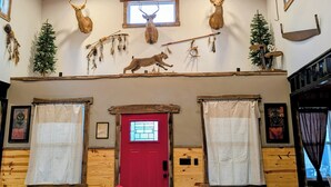 L’intérieur d’une cabane en rondins, avec une porte rouge, des murs en bois, un lustre orné de bois de cerf et des têtes d’animaux fixées au mur.