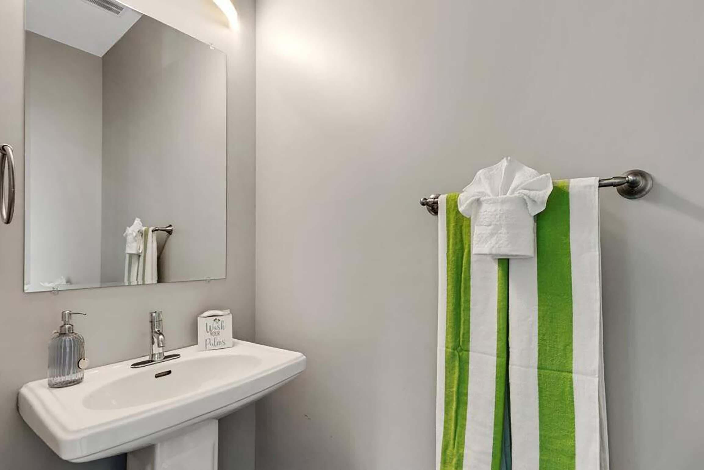 Une salle de bain avec un lavabo blanc, un miroir et un porte-serviettes sur lequel est posée une serviette à rayures vertes et blanches.