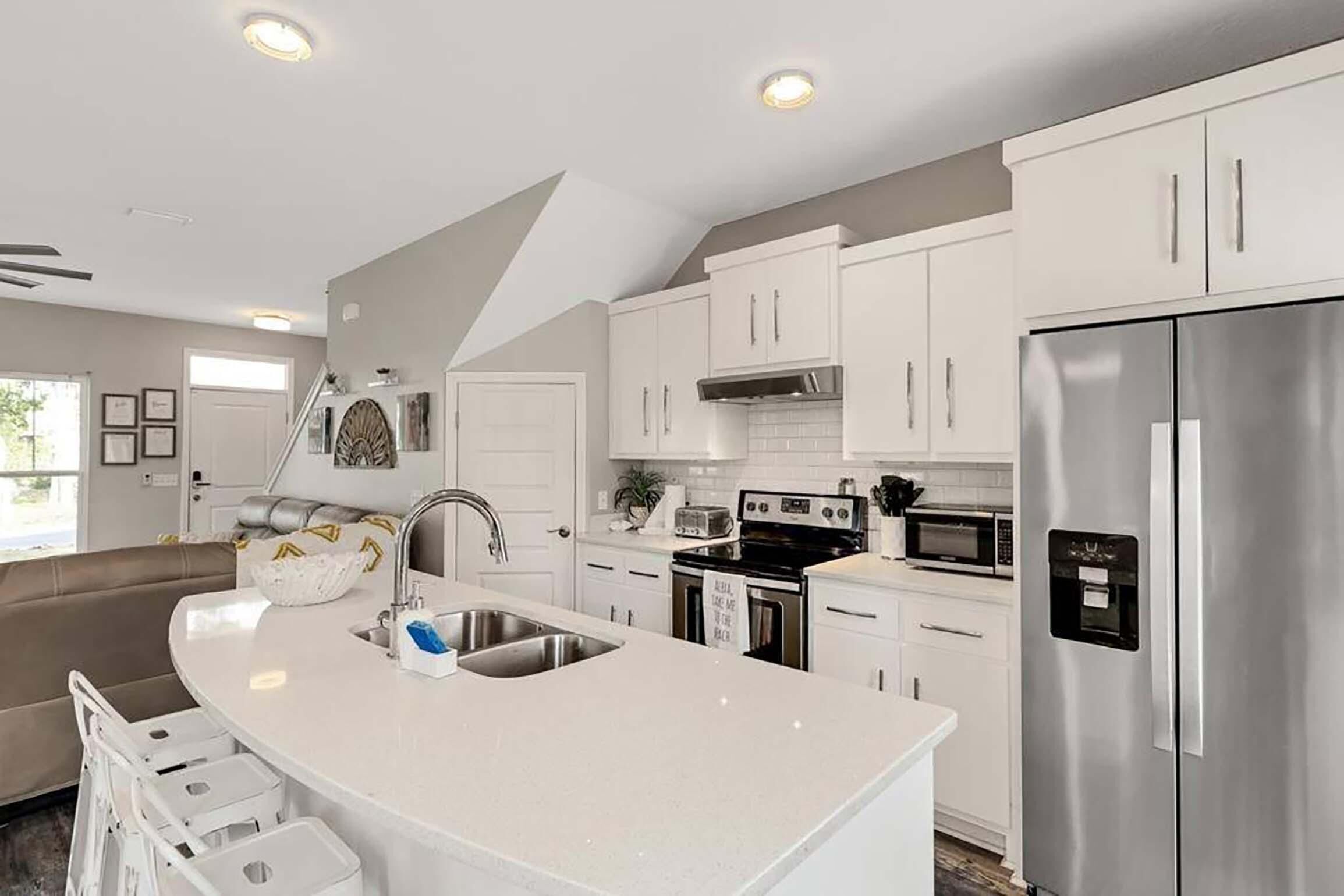 Una cocina moderna con armarios blancos, electrodomésticos de acero inoxidable y una isla curva con un lavamanos.