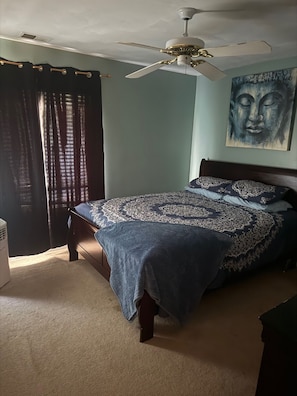 A bedroom with a bed, a ceiling fan, a window with curtains, and a painting on the wall.