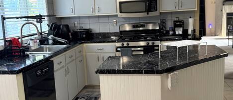Cozinha com armários brancos, bancada preta, micro-ondas de aço inoxidável, fogão e lava-louças.