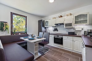 A modern kitchen with white cabinets, a built-in oven, and a dining area with a bench and table.