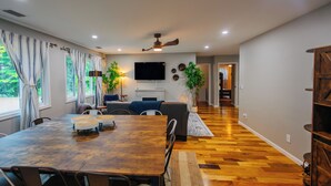 Amplia sala de estar con una mesa de comedor de madera, sofás y un televisor de pantalla plana montado en la pared.