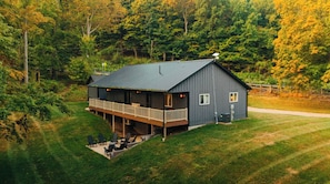 A two-story house with a balcony, surrounded by a grassy yard and dense forest.
