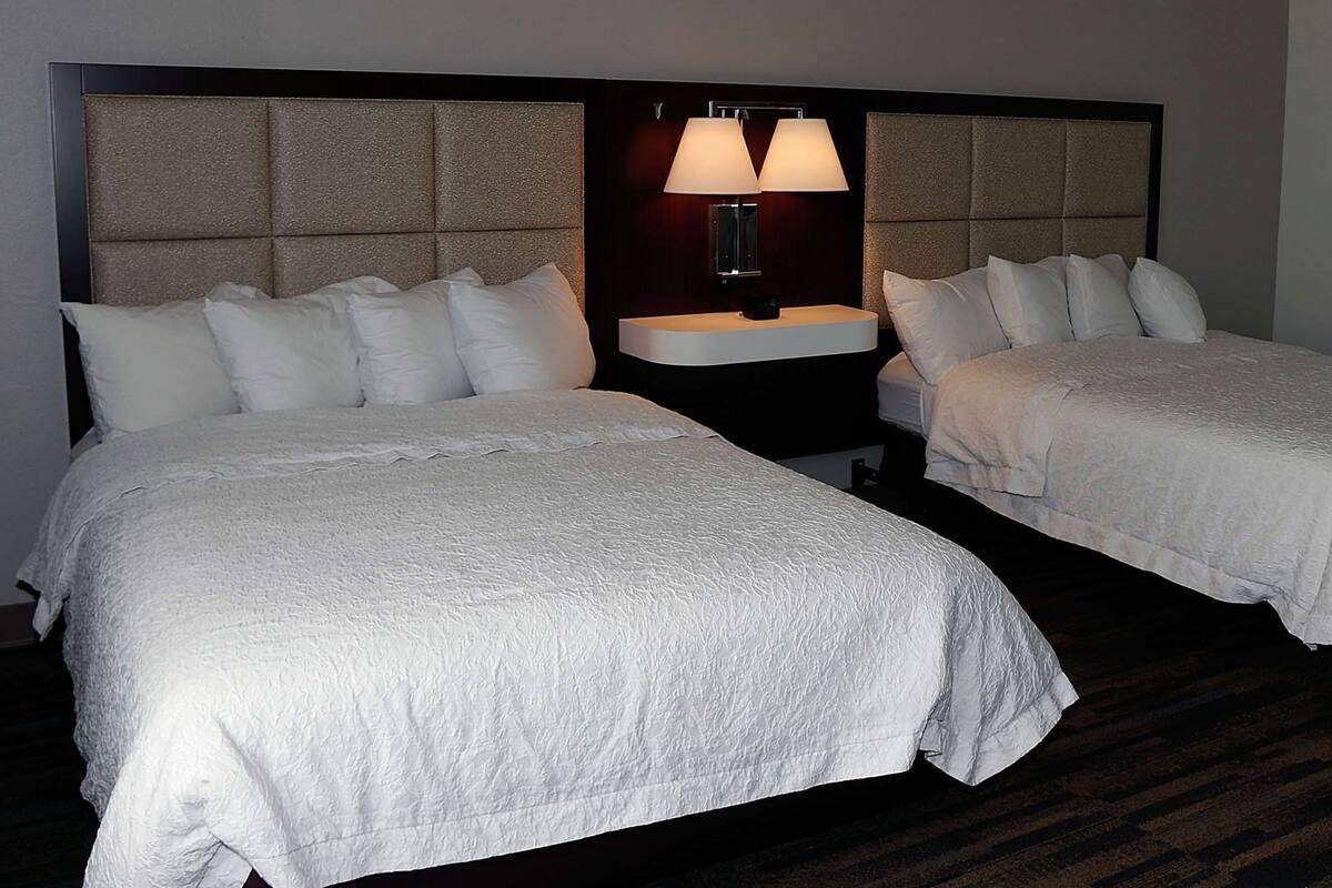 A hotel room with two beds, a nightstand with a lamp, and a headboard with a textured design.