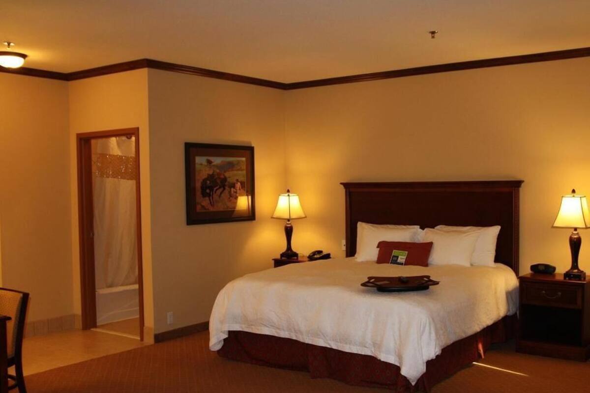 A hotel room with a large bed, two bedside tables, a nightstand, a chair, and a door leading to a bathroom.