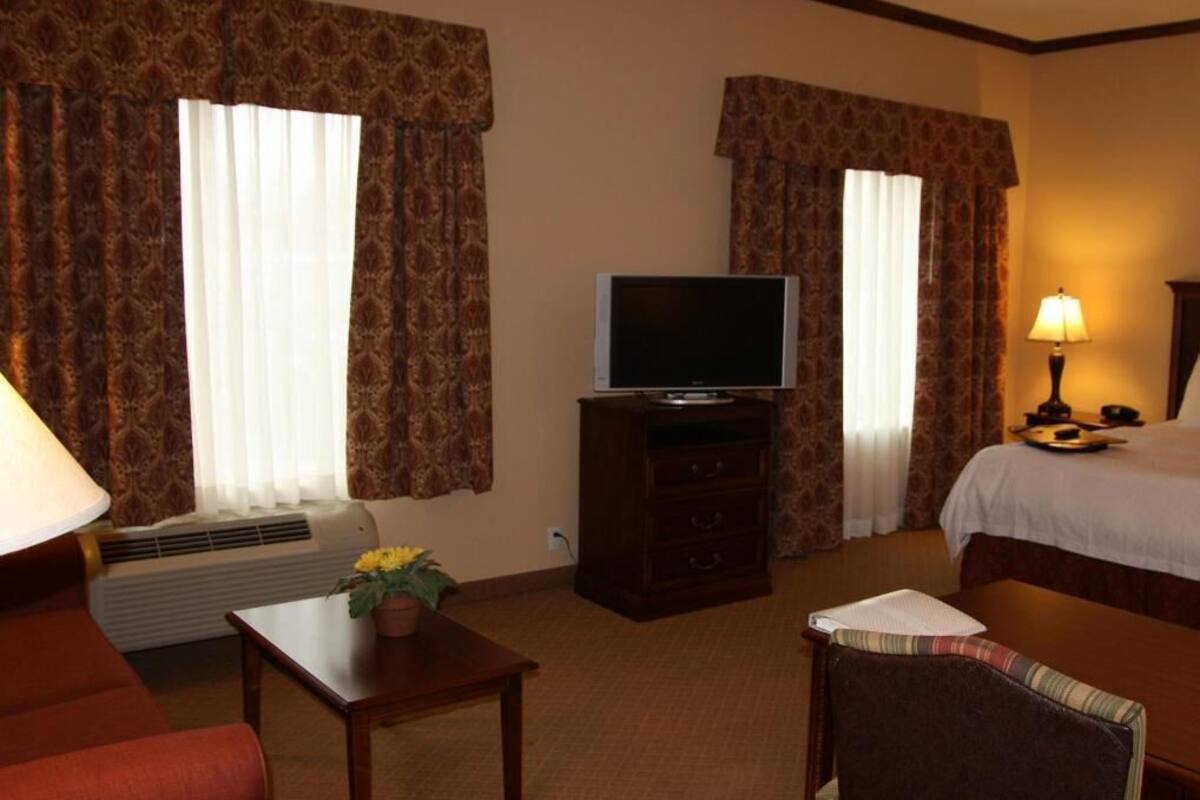 A hotel room with a bed, a television on a dresser, a desk with a lamp, and a chair.