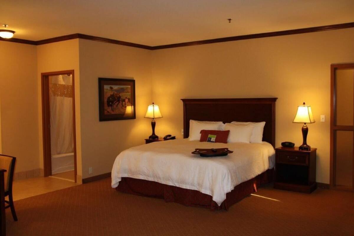 A hotel room with a large bed, two bedside tables with lamps, a framed picture on the wall, and a door leading to a bathroom.