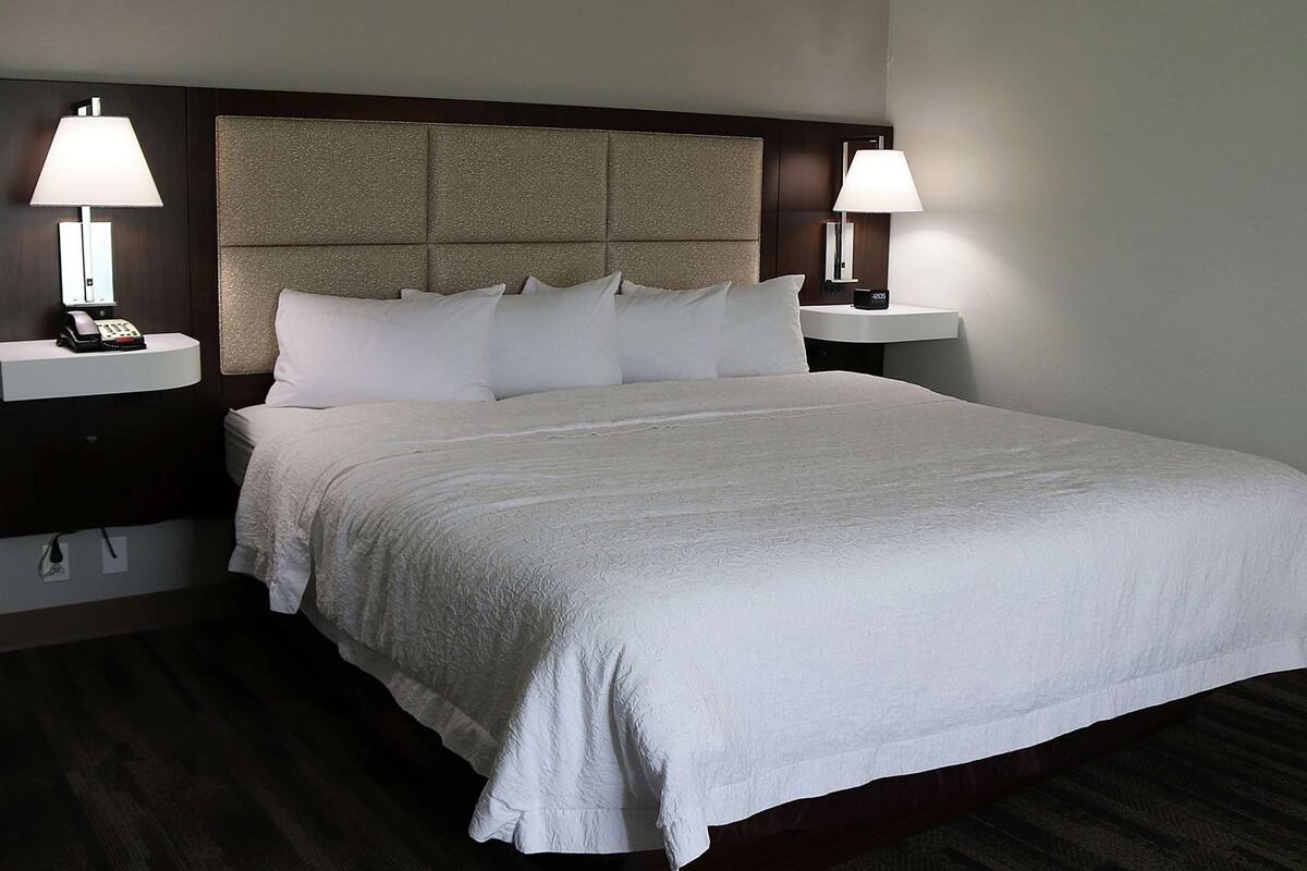 A hotel room with a large bed, two bedside tables with lamps, a telephone, and a headboard with a textured panel.