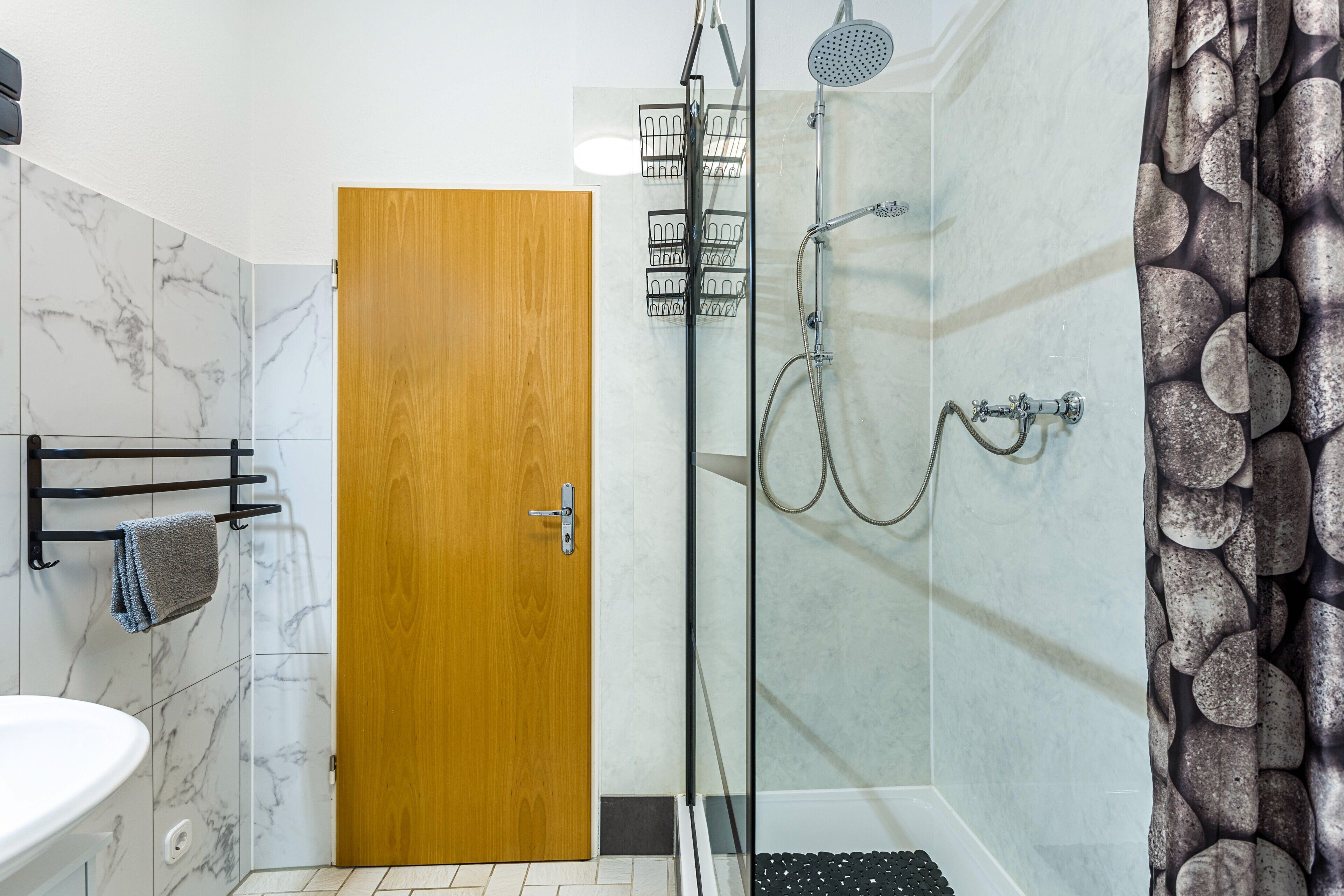 Une salle de bain avec un mur en marbre, une porte en bois, une cabine de douche en verre et un lavabo.