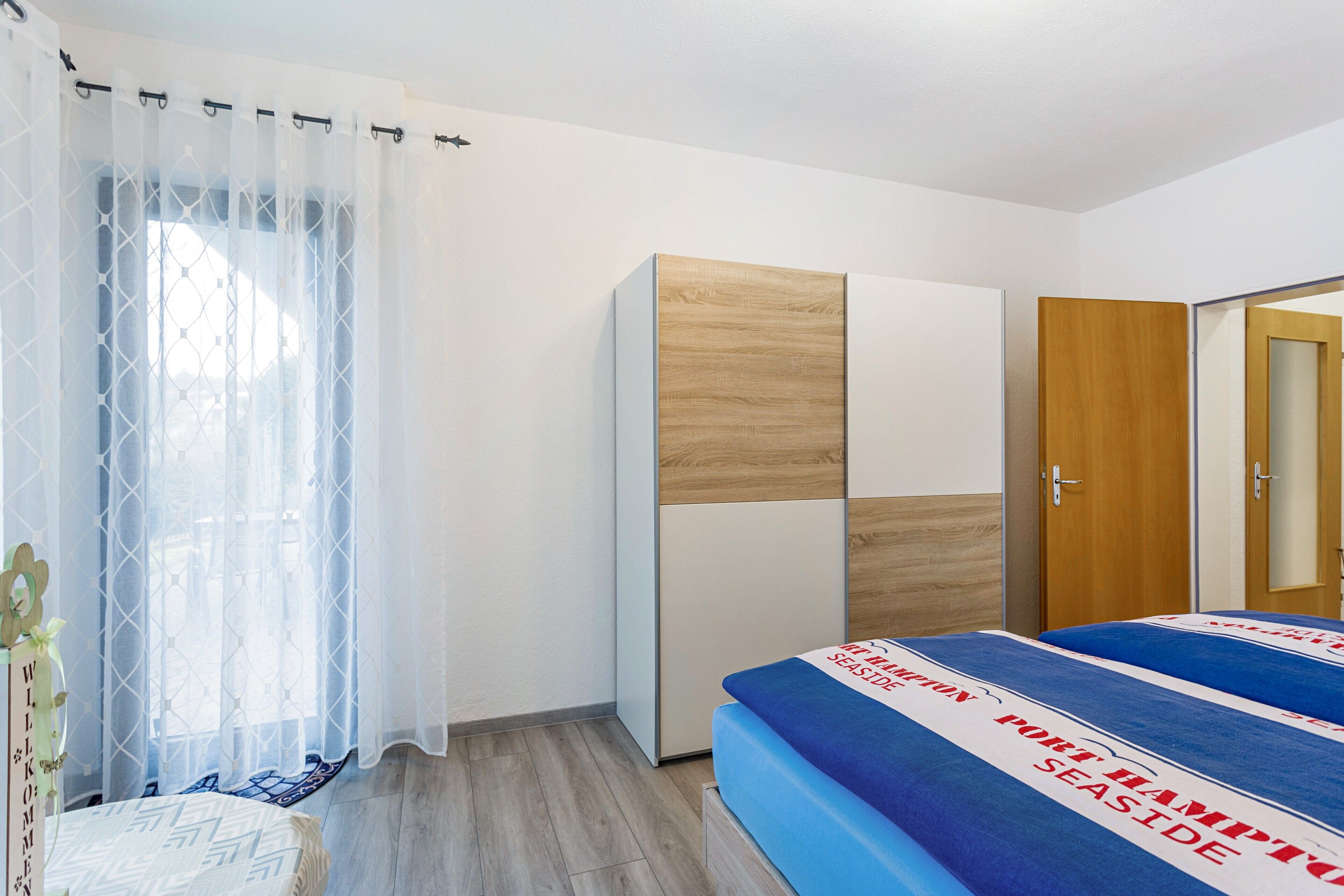 A bedroom with a bed, wardrobe, and a window with curtains.