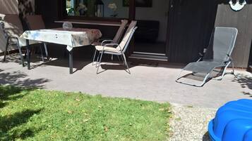 En uteplats med ett bord och stolar, en överbyggd sittplats, en blå uppblåsbar pool och en dekorativ vägg med ett ankarmotiv.