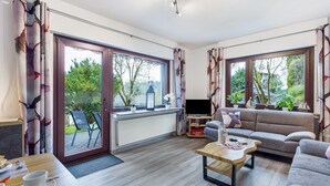 A living room with a sofa, TV, and a dining area with chairs and a table. - Apartment 'Astrid' with Private Terrace, Garden, and Wi-Fi (Sundern (Sauerland))