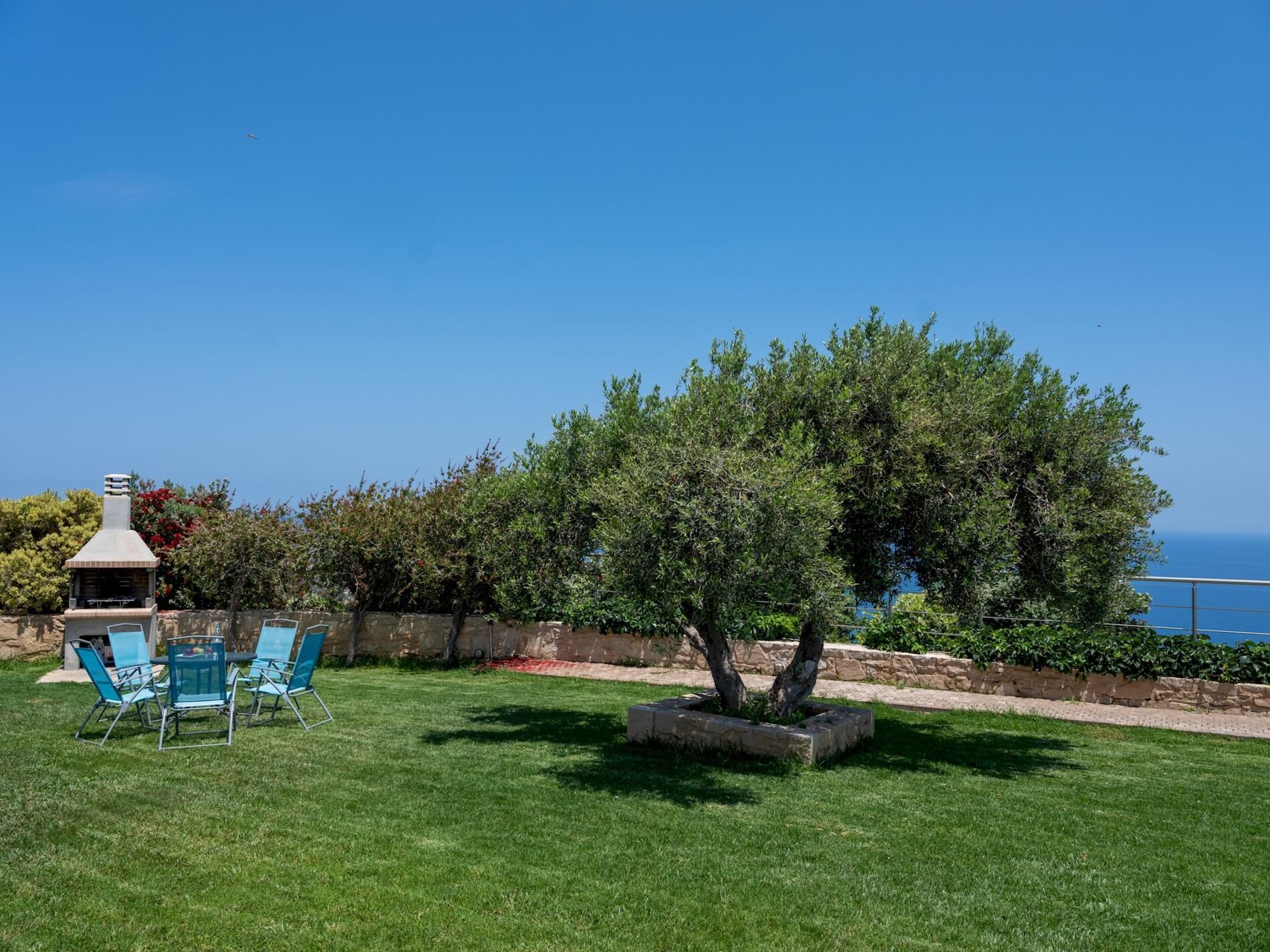 A backyard with a barbecue grill, outdoor seating, and a view of the ocean.