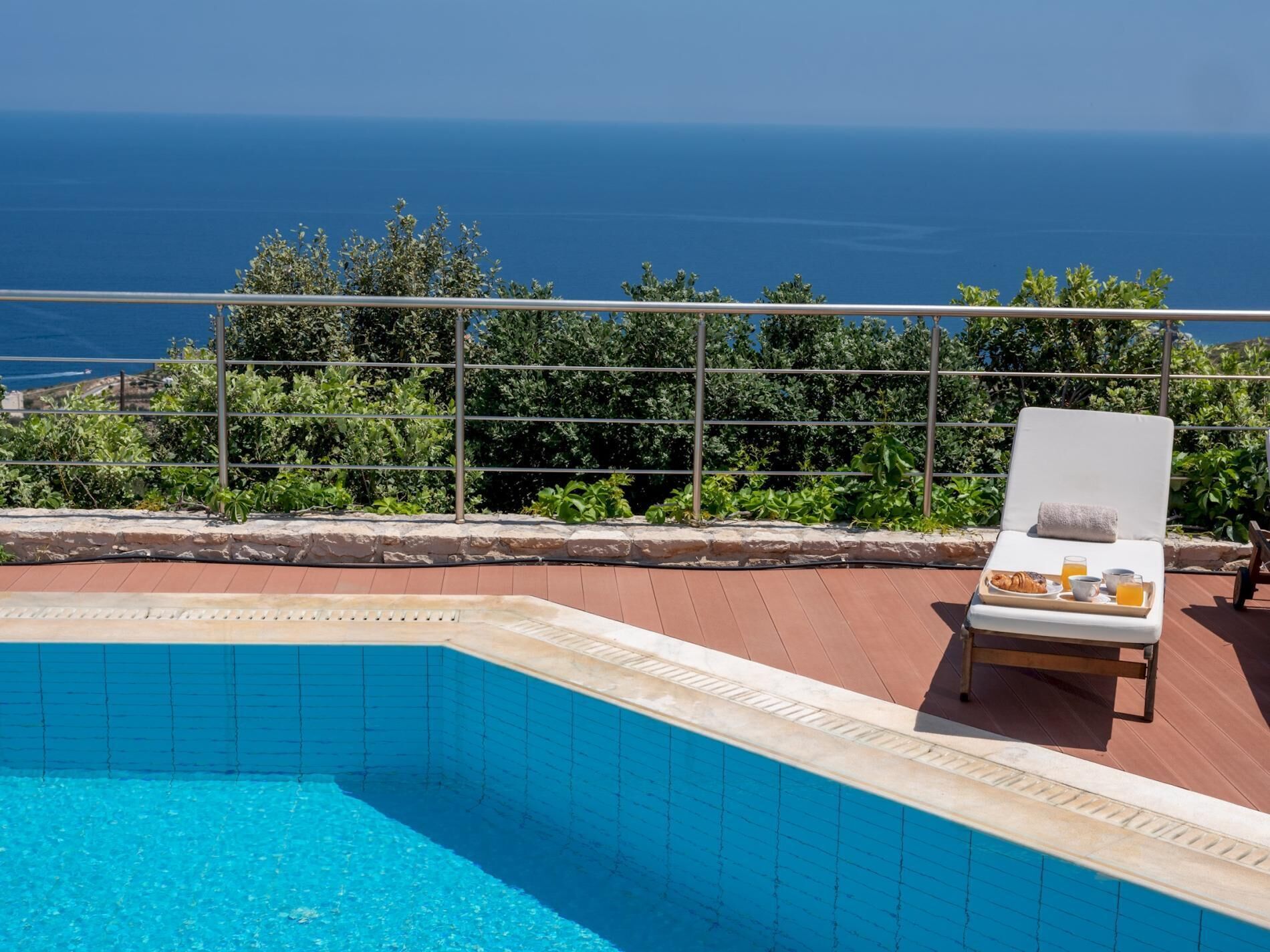 Una zona de piscina amb una cadira relaxant, un plat amb articles per esmorzar, i vista al mar.