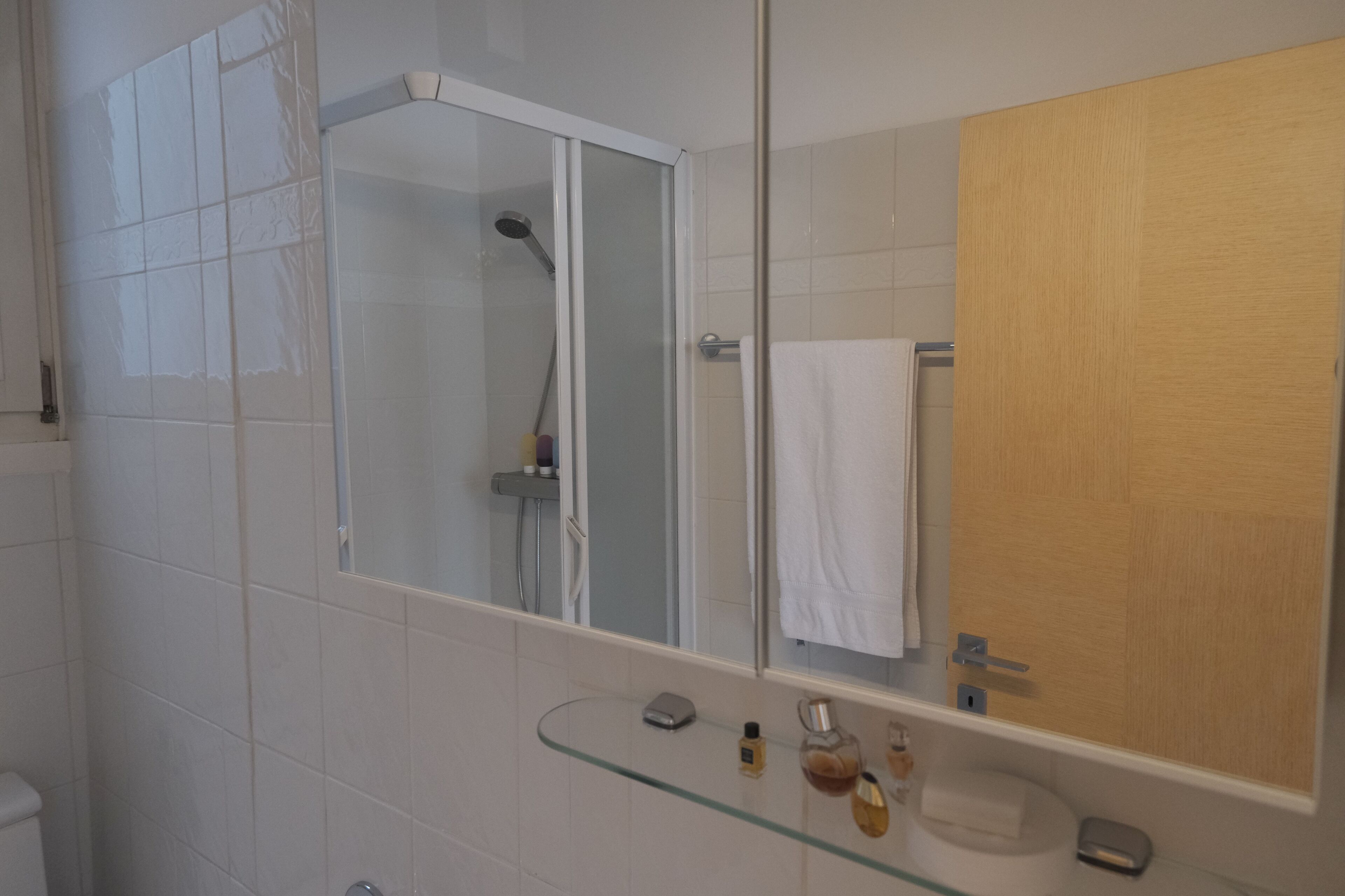 A modern bathroom with a glass shower enclosure, a wooden door, and a glass sink.
