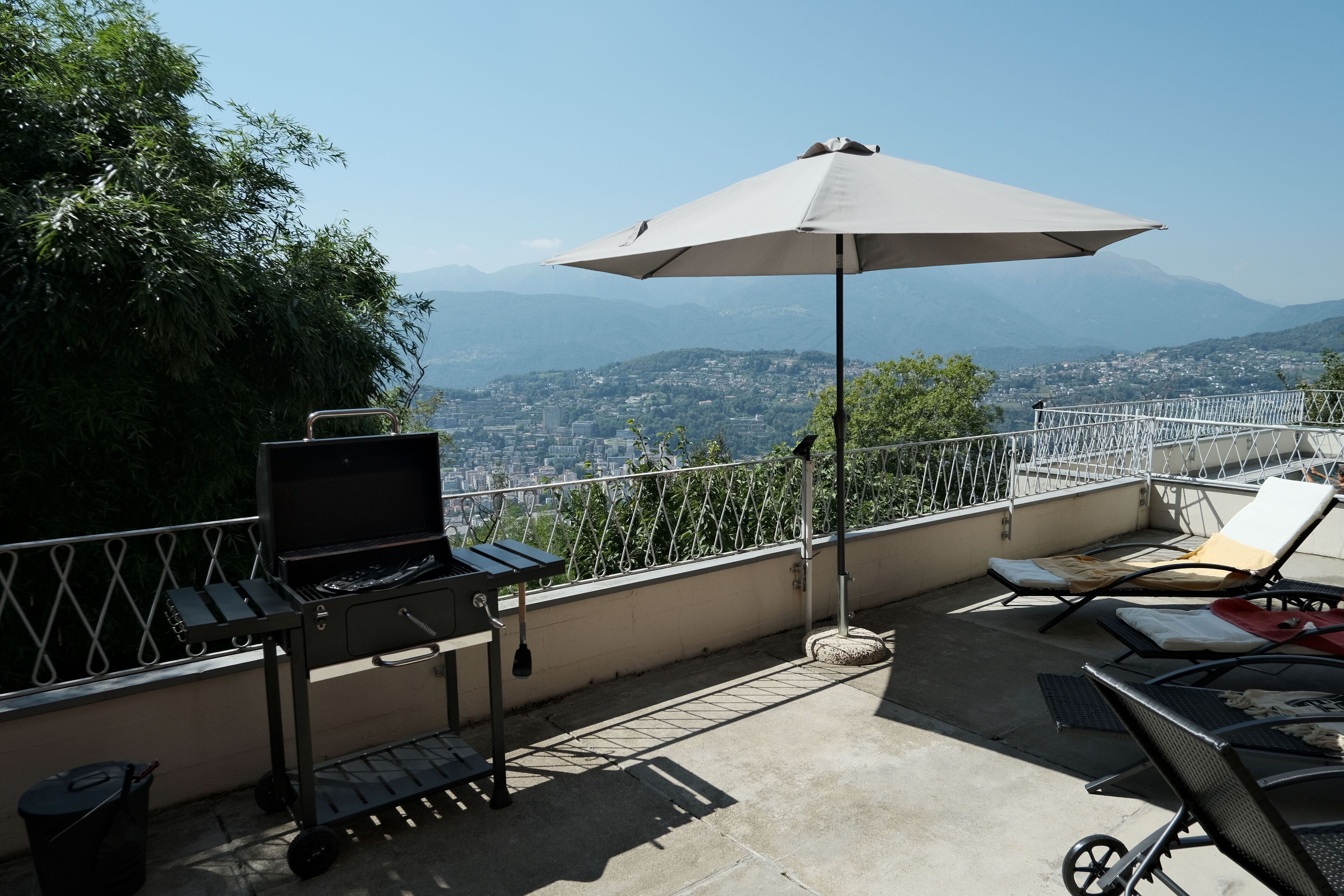 Terraza en la azotea con una parrilla, sillones de descanso y vistas a la ciudad y montañas.