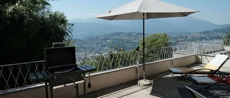 Terraza en la azotea con una parrilla, sillones de descanso y vistas a la ciudad y montañas.
