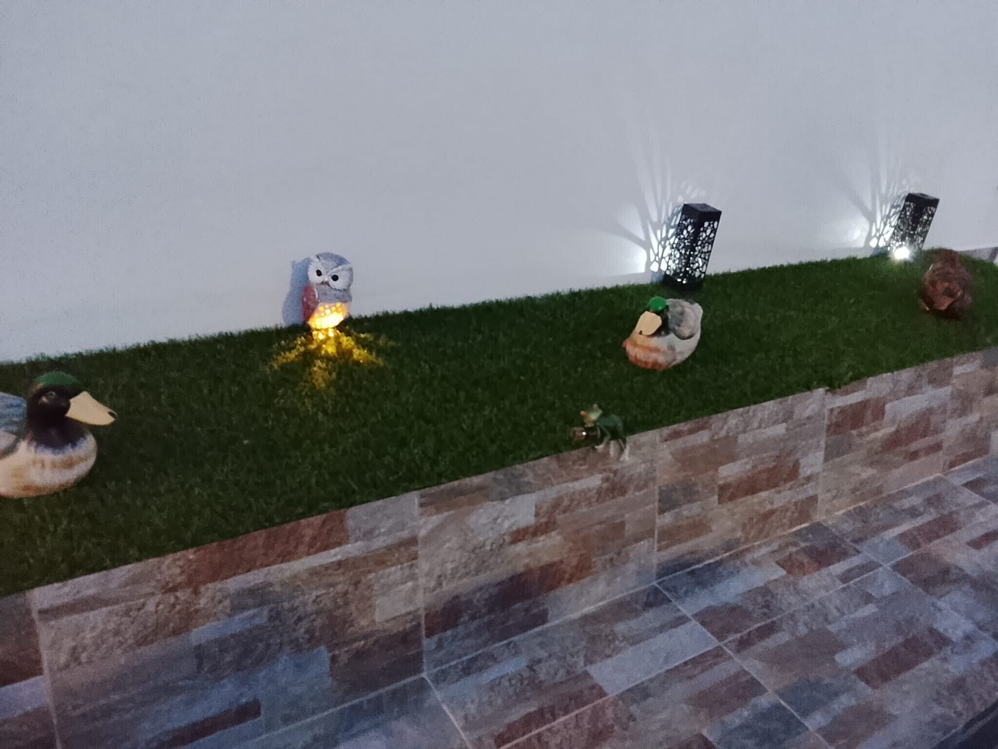 Un jardín con patos ornamentales, un comedero para pájaros y un aplique de pared.