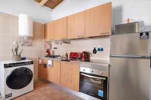 A kitchen with wooden cabinets, a stainless steel refrigerator, a washing machine, and a microwave.