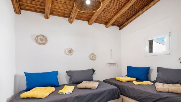 A room with two beds, wooden ceiling beams, a small window, and wall decor.