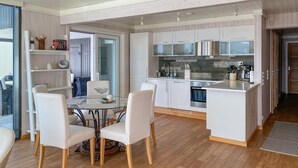 Une cuisine moderne avec des meubles blancs, un îlot central et un coin repas comprenant une table et des chaises en verre.